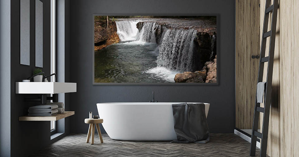Modern, minimalist bathroom shows a waterfall scene on a wall-mounted TV above a large, free-standing bathtub