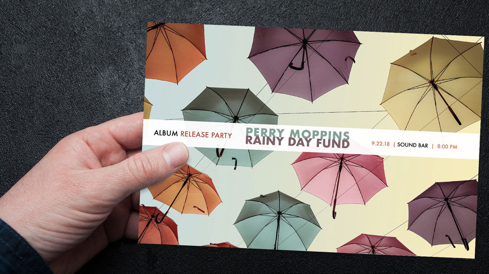 Hand holds postcard for Perry Moppins Rainy Day Fund album release party with colorful floating umbrellas in the background.