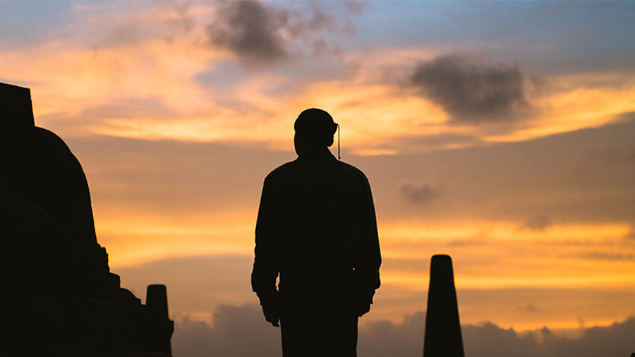 Silhouette of the back of a person walking with a dramatic orange sunset