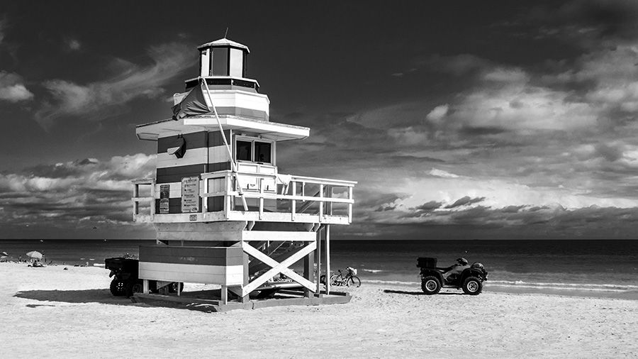 Dramatic black and white photograph of lifeguard tower on the beach shows sky appearing stormy.