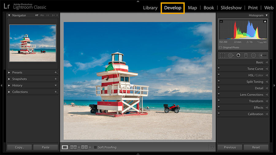 Vibrant colorful photograph of lifeguard tower on the beach with bright blue water and clear, sunny sky with wispy clouds.