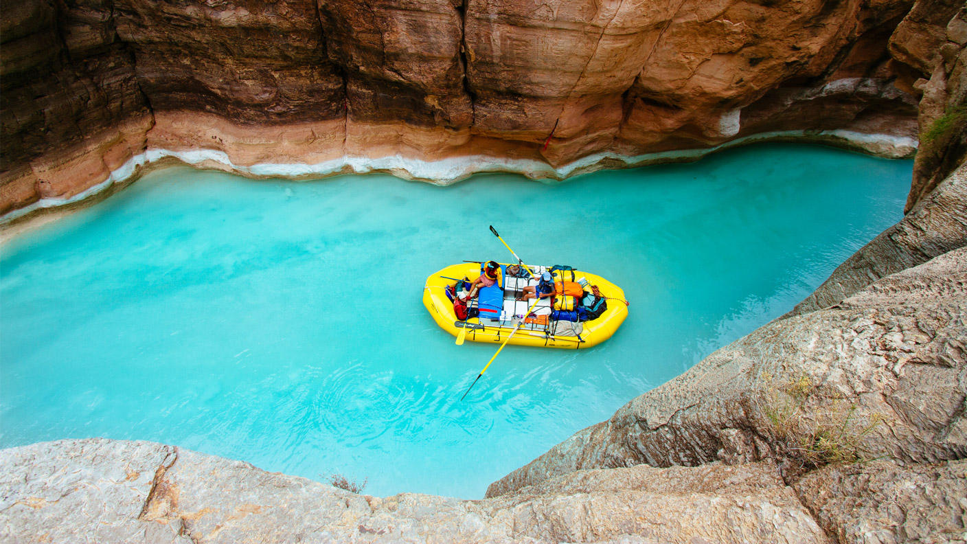 Two people floating on inflatable raft between canyon walls, water is clear light blue