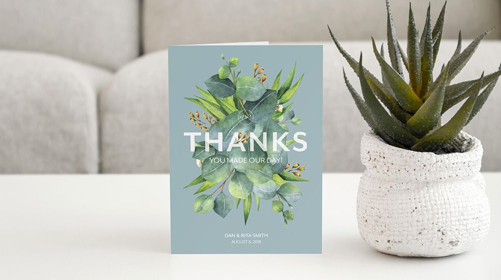Custom thank you card featuring greenery sits on a coffee table next to potted succulent.  