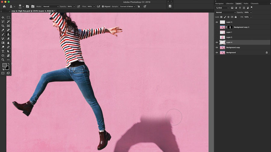 Woman jumping into the air with pink backdrop. Shadow is being erased using the Healing Brush tool in Adobe Photoshop. 