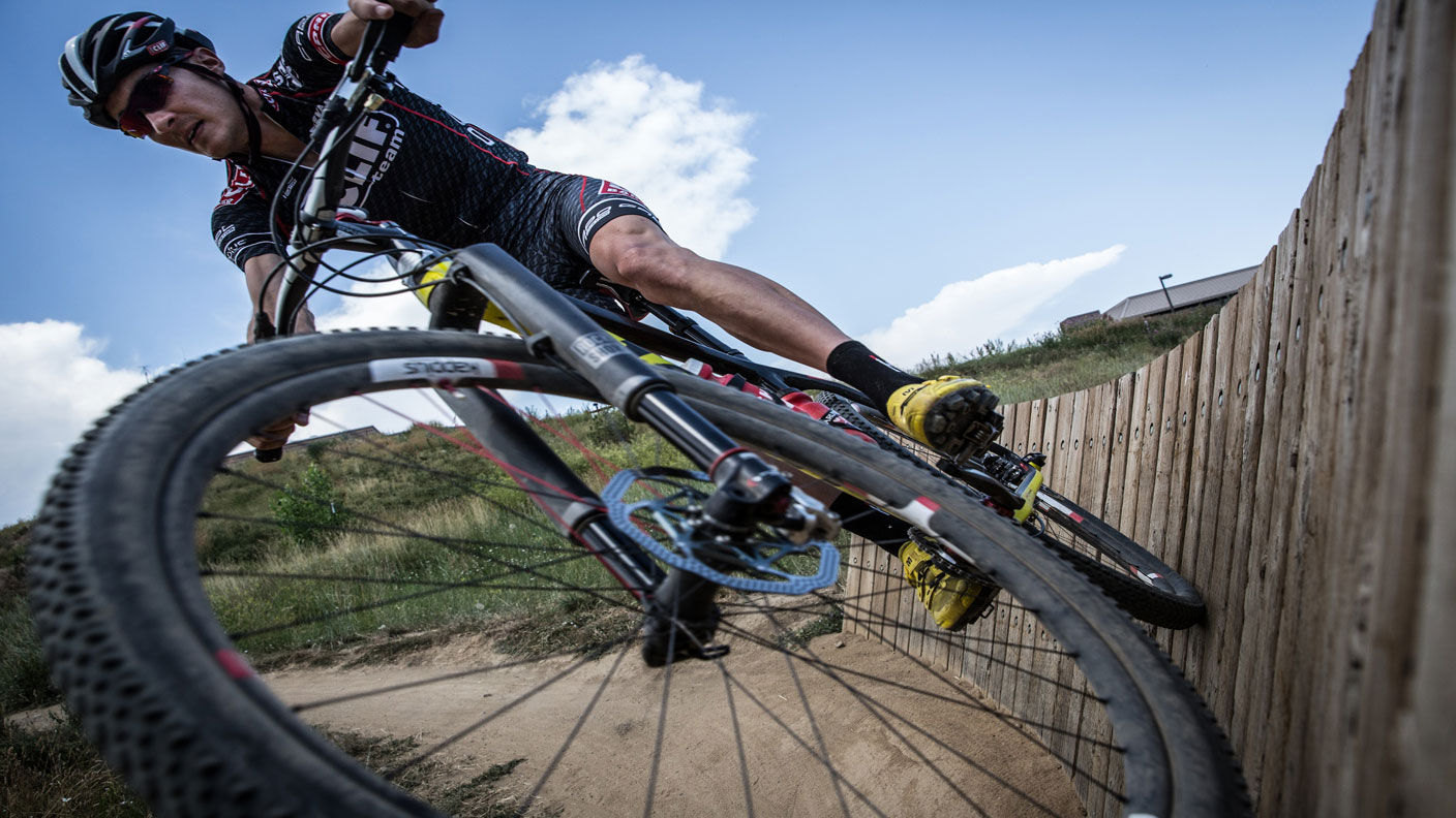Extreme bicyclist rides his bike horizontally along a wooden fence.