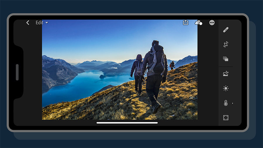 Edited photo of backpackers on a mountain with a lake appears on a mobile phone.