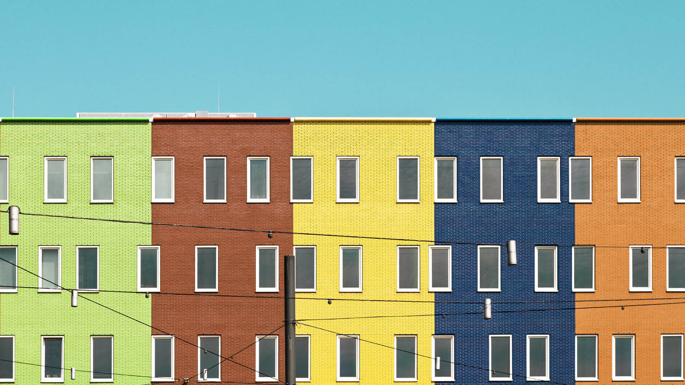 Adjoining hi-rise buildings painted green, red, yellow, blue, and orange against a pale blue sky with electric wires in front
