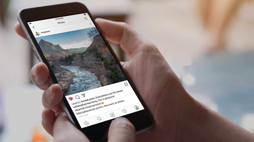 Person holding mobile phone with social media image of canyon and river. 