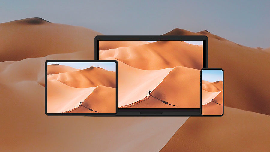 Photo of a sand dune with the same image on an pad, phone, and a laptop