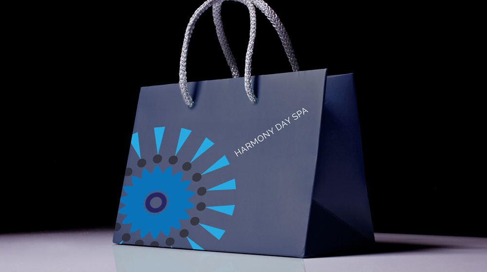 Blue flower and geometric patterned logo for Harmony Day Spa appears on a gray bag. 