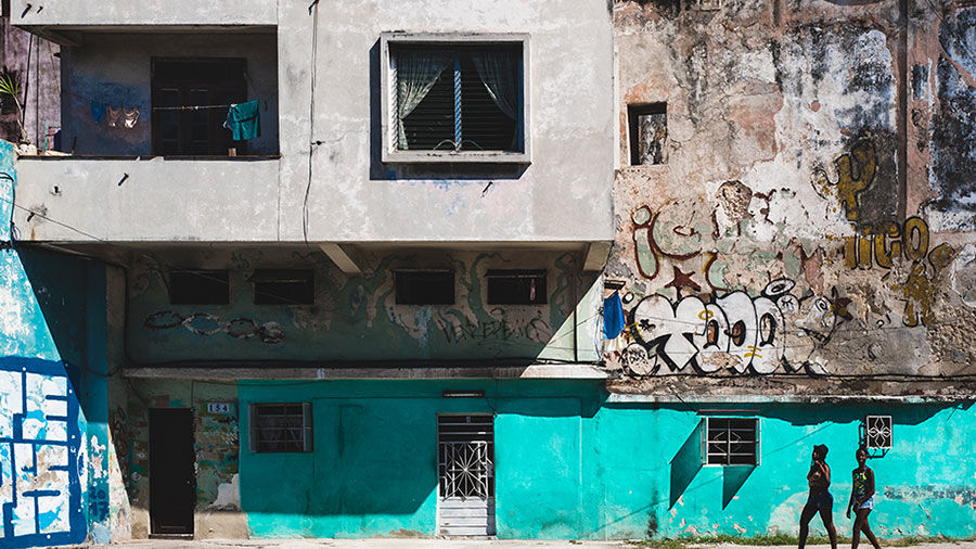 Photo of two people walking by a dilapidated and colorful building with graffiti