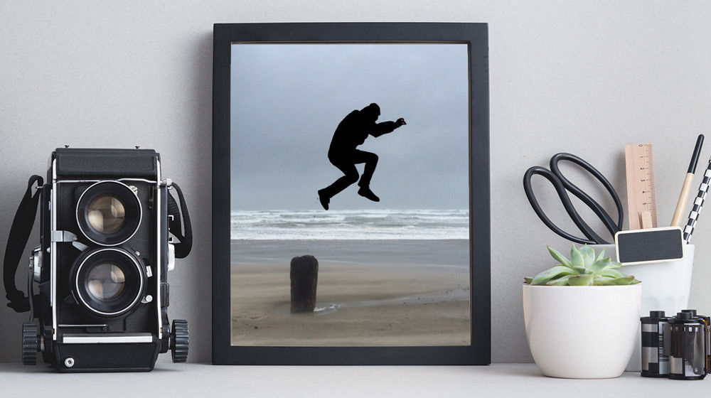 Silhouette of a man jumping over a post on the beach.