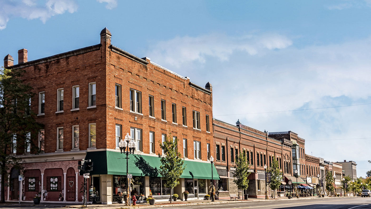 Perspective view of large building with green awning next to smaller shops on tree-lined downtown boulevard
