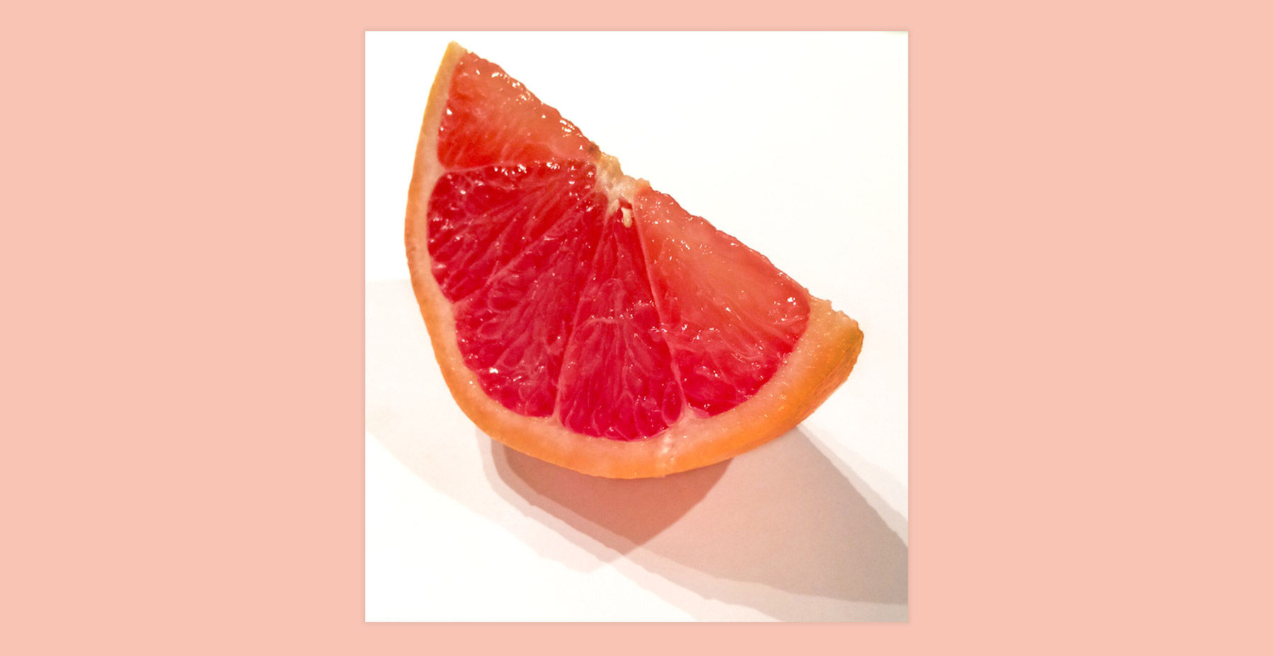 A photograph of a grapefruit wedge with shadows on a white background
