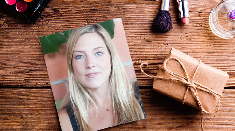 Woman’s portrait sits on a wooden table with makeup and a small package. 