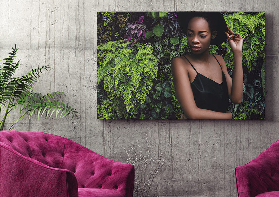 Picture of model in front of new background with green plants placed on a wall behind two fuchsia-colored chairs
