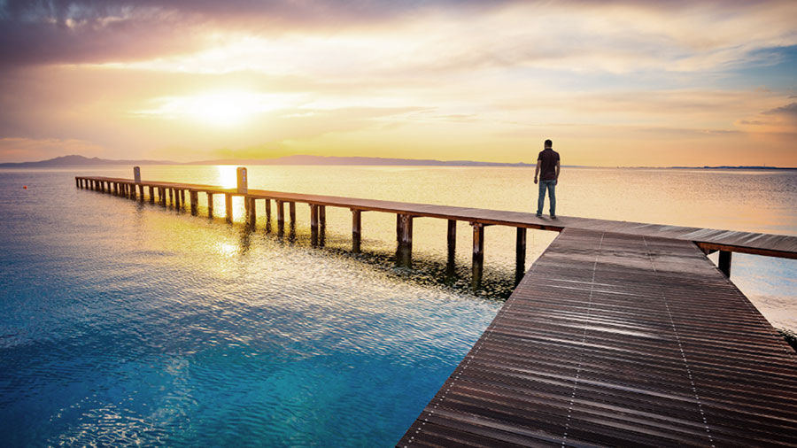 Photograph of a man standing on a bridge over the ocean watching the sun rise