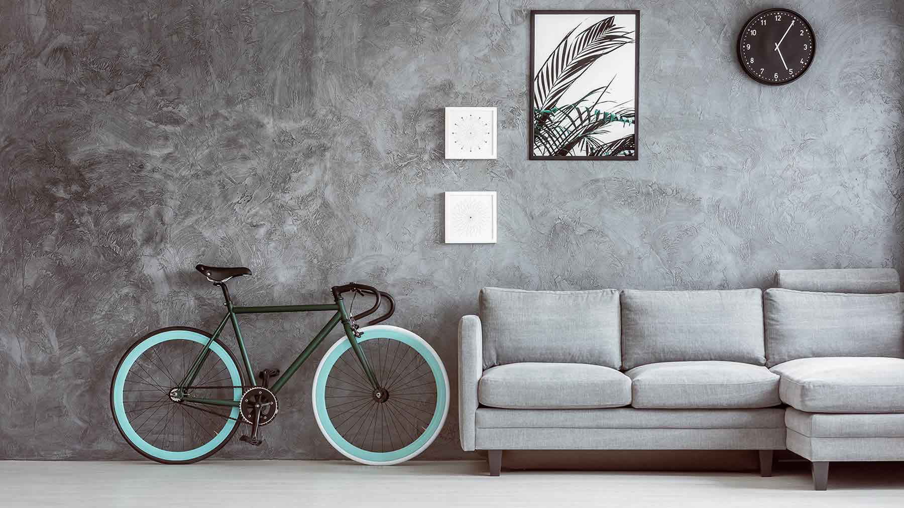 Racing bicycle leans against gray interior wall. Gray couch, black clock, and white and black artwork hang on the wall.
