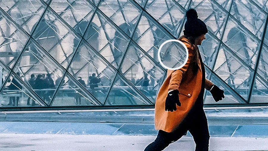 A person walking in winter clothing past a glass building with a white circle highlighting an area of the image