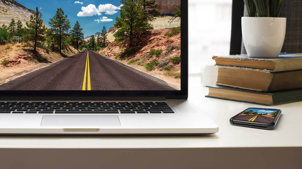 A computer on a desk displays a photograph of a road in a desert landscape.