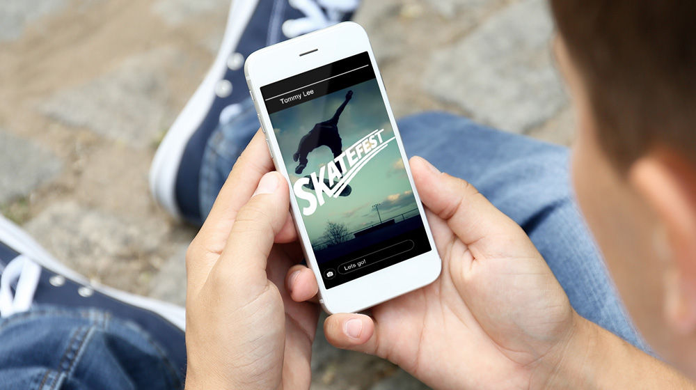 Teenager holds a mobile phone displaying a skateboarder with the word “SKATEFEST” 
