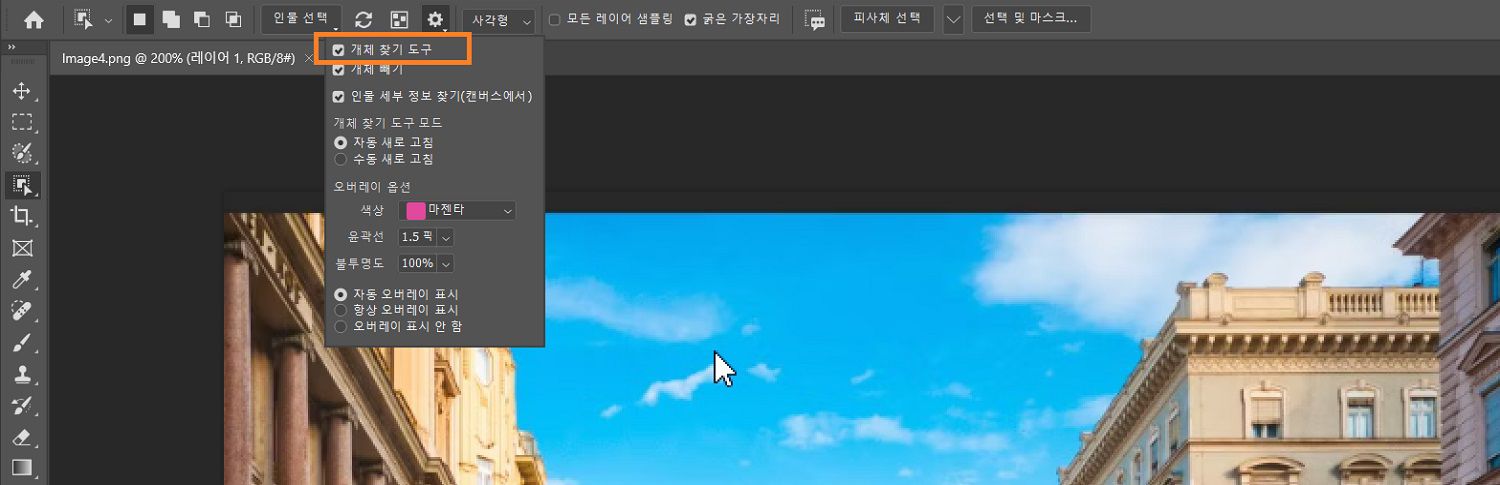 Photoshop 캔버스의 건물 이미지 위에 있는 옵션 표시줄에서 오브젝트 선택 도구의 설정 메뉴에 오브젝트 찾기가 강조 표시되어 있습니다.