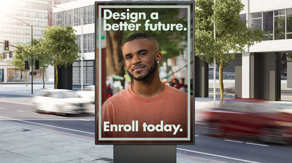 ชายหนุ่มวัยมหาลัยเป็นนายแบบอยู่บนโปสเตอร์ที่มีข้อความ “Design a better future Enroll today” 
