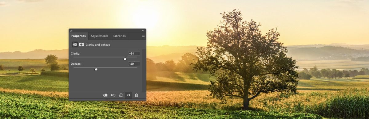 Napfényes vidéki táj zöld mezőkkel, magányos fával és ködös horizonttal. A Photoshop korrekciós paneljén a Tisztaság beállítás értéke +61, a Ködfátyol eltávolítása beállításé pedig -29
