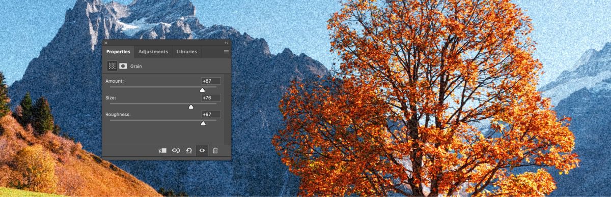 Az Adobe Photoshop felhasználói felülete a Szemcsézettség korrekciós réteg tulajdonságpaneljével, amelyen a Mérték, a Méret és a Durvaság csúszka nagy értékre vannak állítva, és egy havas hegyet, őszi fákat és füves domboldalt ábrázoló tájképre van alkalmazva