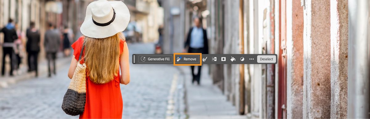 Esta es una imagen de la aplicación de Photoshop en el escritorio, que muestra la barra de tareas contextual con la opción Quitar resaltada sobre un área seleccionada. Una mujer con sombrero y un vestido camina por una calle adoquinada. 