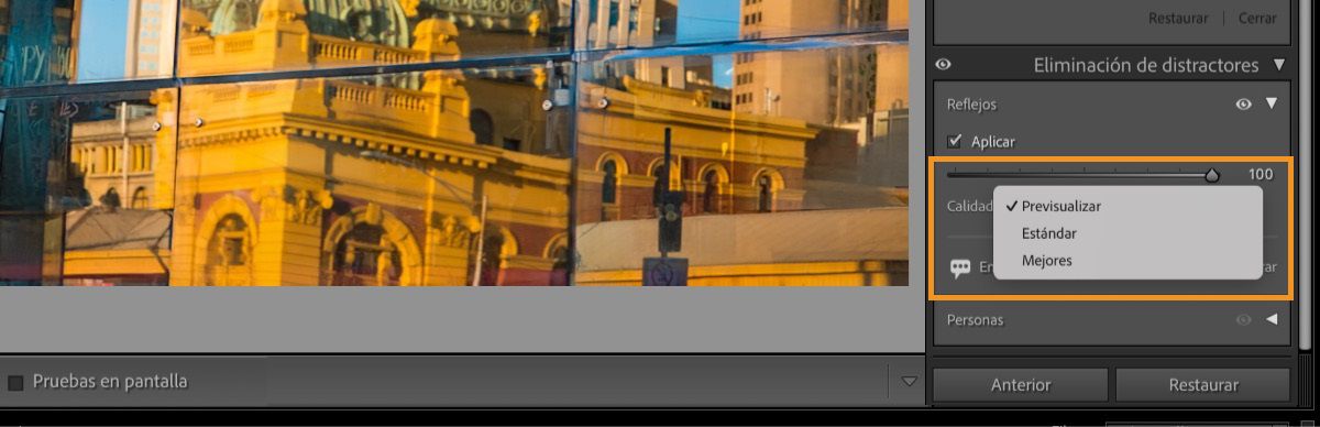 Captura de pantalla de una interfaz de software de edición de fotos que muestra un paisaje urbano reflejado en ventanas de cristal. El reflejo muestra edificios amarillos y anaranjados con columnas y arcos. Un panel &quot;Eliminación de distracción&quot; de la derecha tiene activada la opción &quot;Reflejos&quot;, con la calidad definida en 100, y las opciones &quot;Previsualización&quot;, &quot;Estándar&quot; y &quot;Óptima&quot;. Los botones con las etiquetas &quot;Anterior&quot; y &quot;Restablecer&quot; se encuentran debajo del panel.